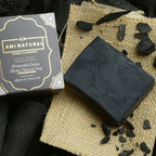 AMI NATURAL ACTIVATED CHARCOAL SOAP bar in black with rough texture and packaging featuring gold and white text on dark background