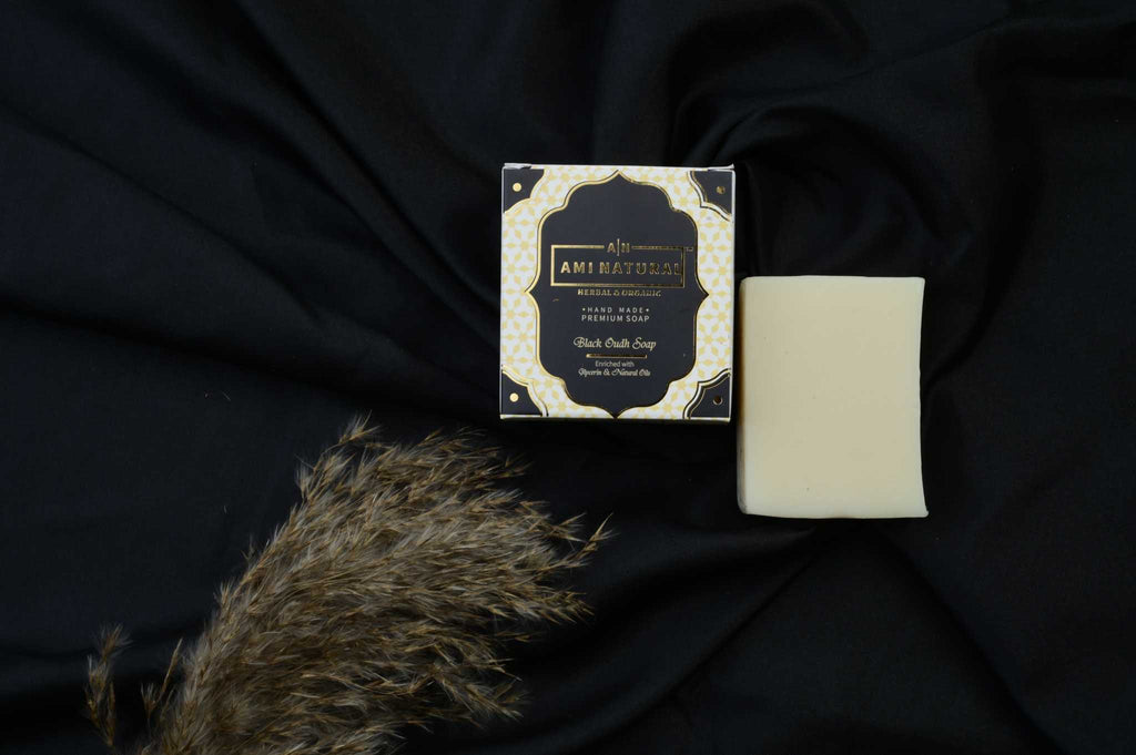 AMI NATURAL BLACK OUDH SOAP with elegant black and gold packaging alongside a plain off-white soap bar on black fabric