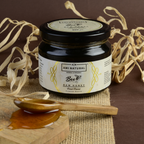 Ami Natural Raw Fennel Honey in a dark glass jar with a black lid, white label featuring herbal design, next to wooden spoon and honey drizzle